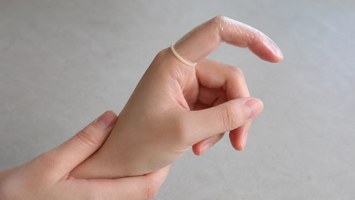 Adult hand gently bending a finger while checking that a transparent finger condom stays in place
