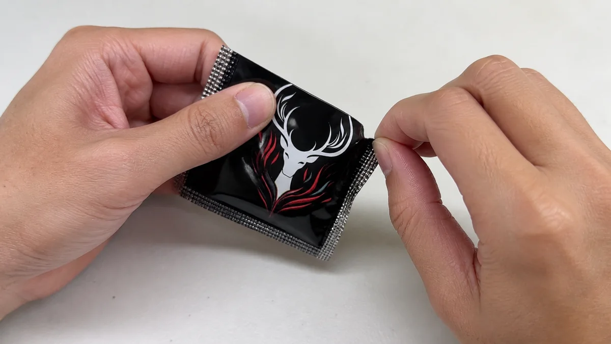 Adult hands using finger pads to make a small controlled tear at the edge of a black finger condom packet